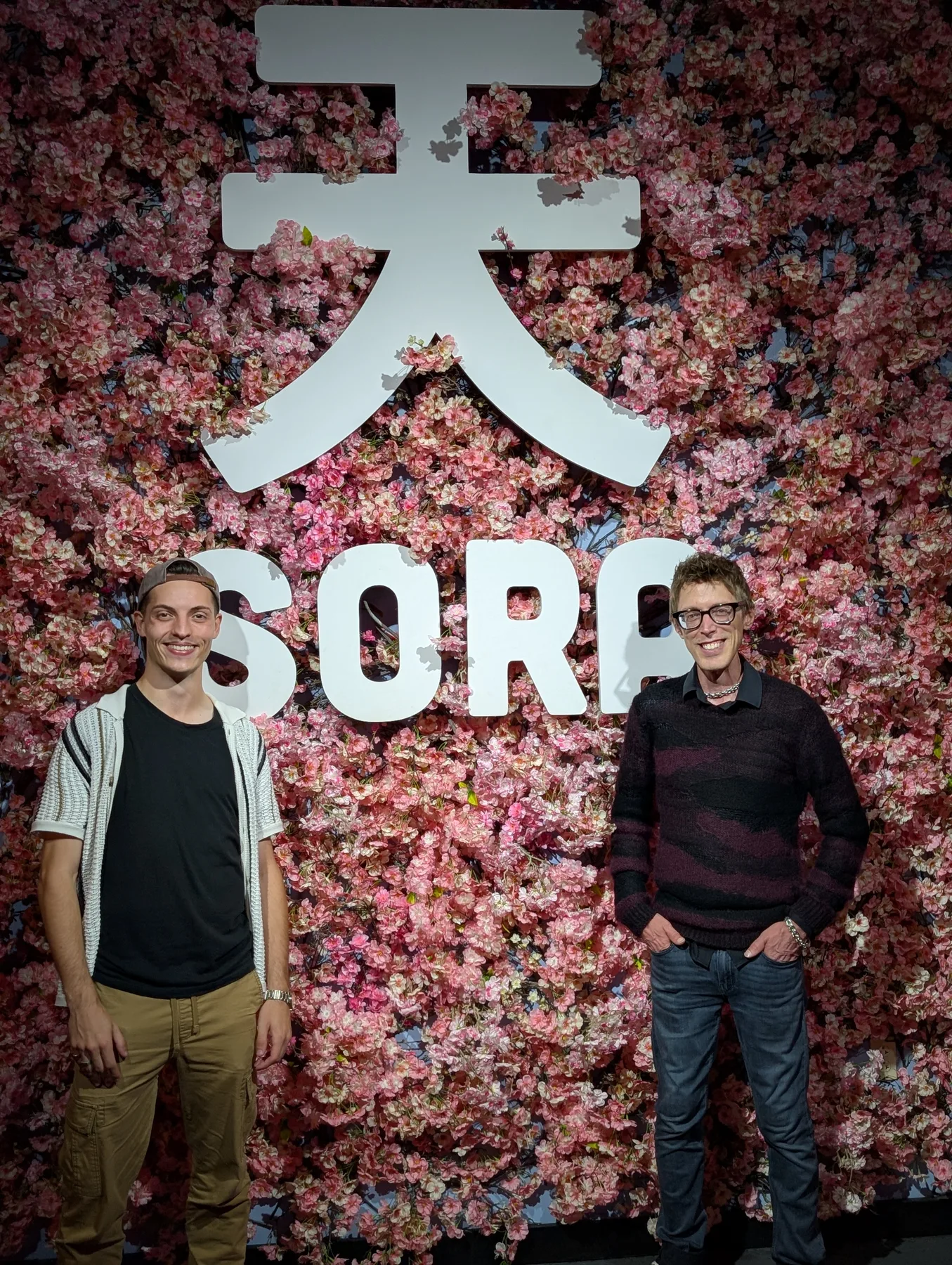 Two OpenCLE guests standing in front of the Sora flower wall
